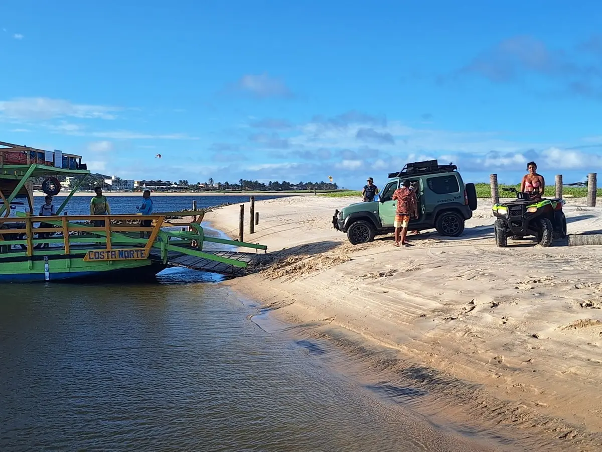 Balsa de madeira atracada na areia, com carro e quadriciclo desembarcando